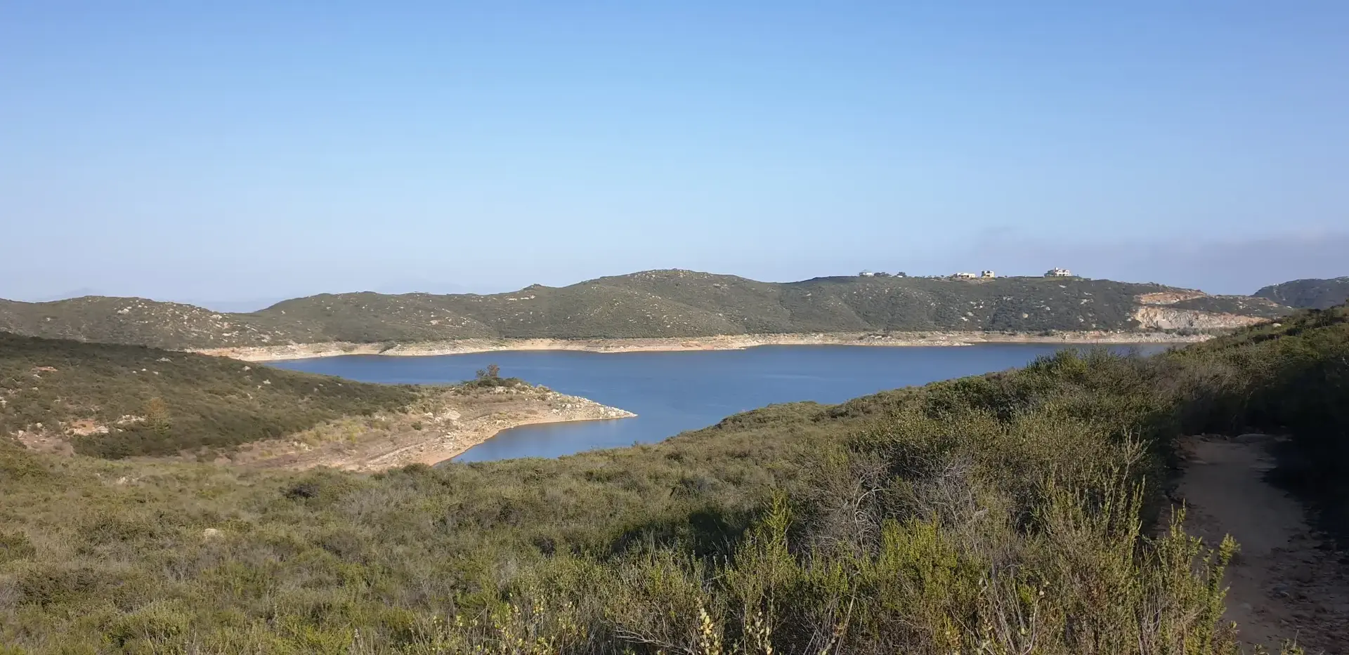 Panoramic view of a calm blue lake surrounded by green and brown hills.