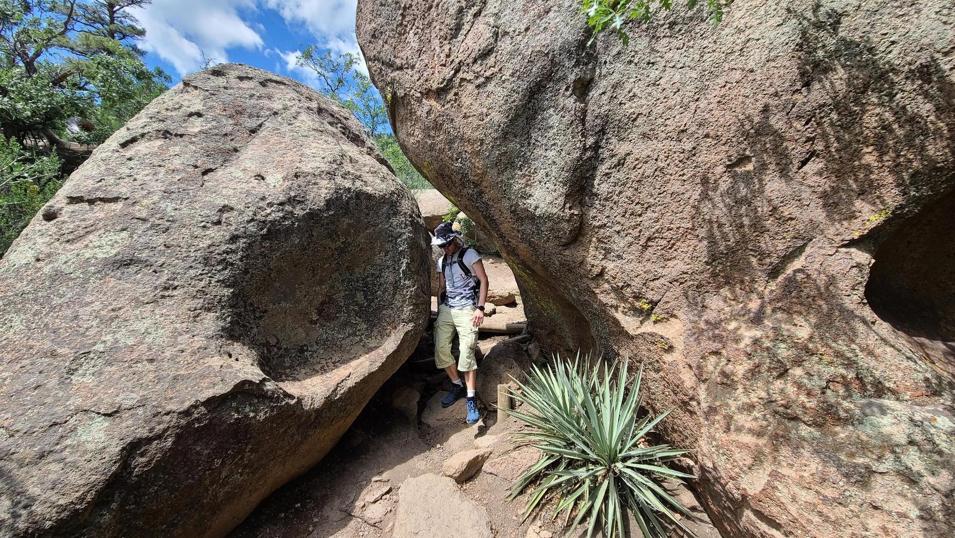 Hiker walking between two large boulders on a sunny, rocky trail.