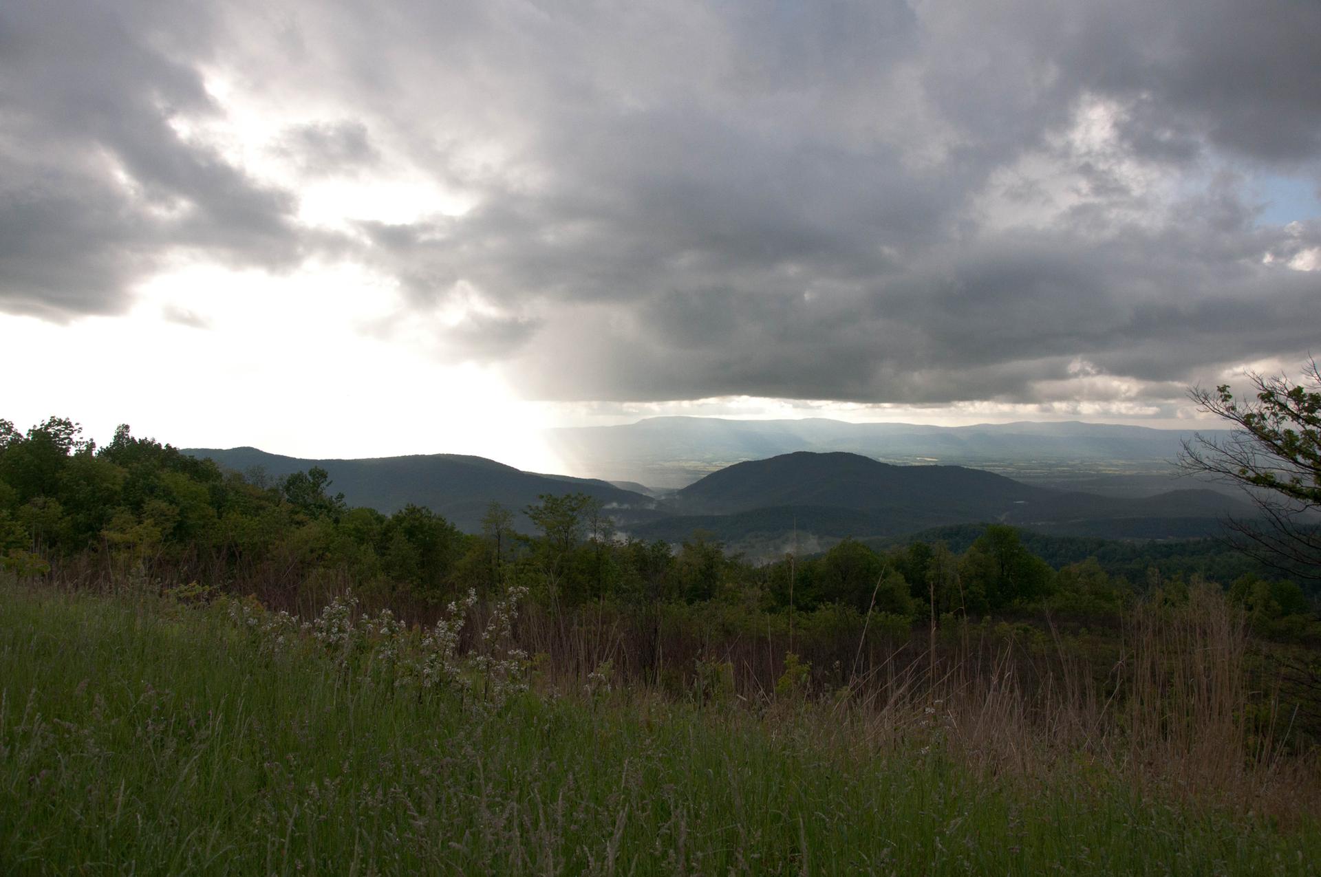 Dramatic cloudy sky over mountains, with sun breaking through onto landscape.