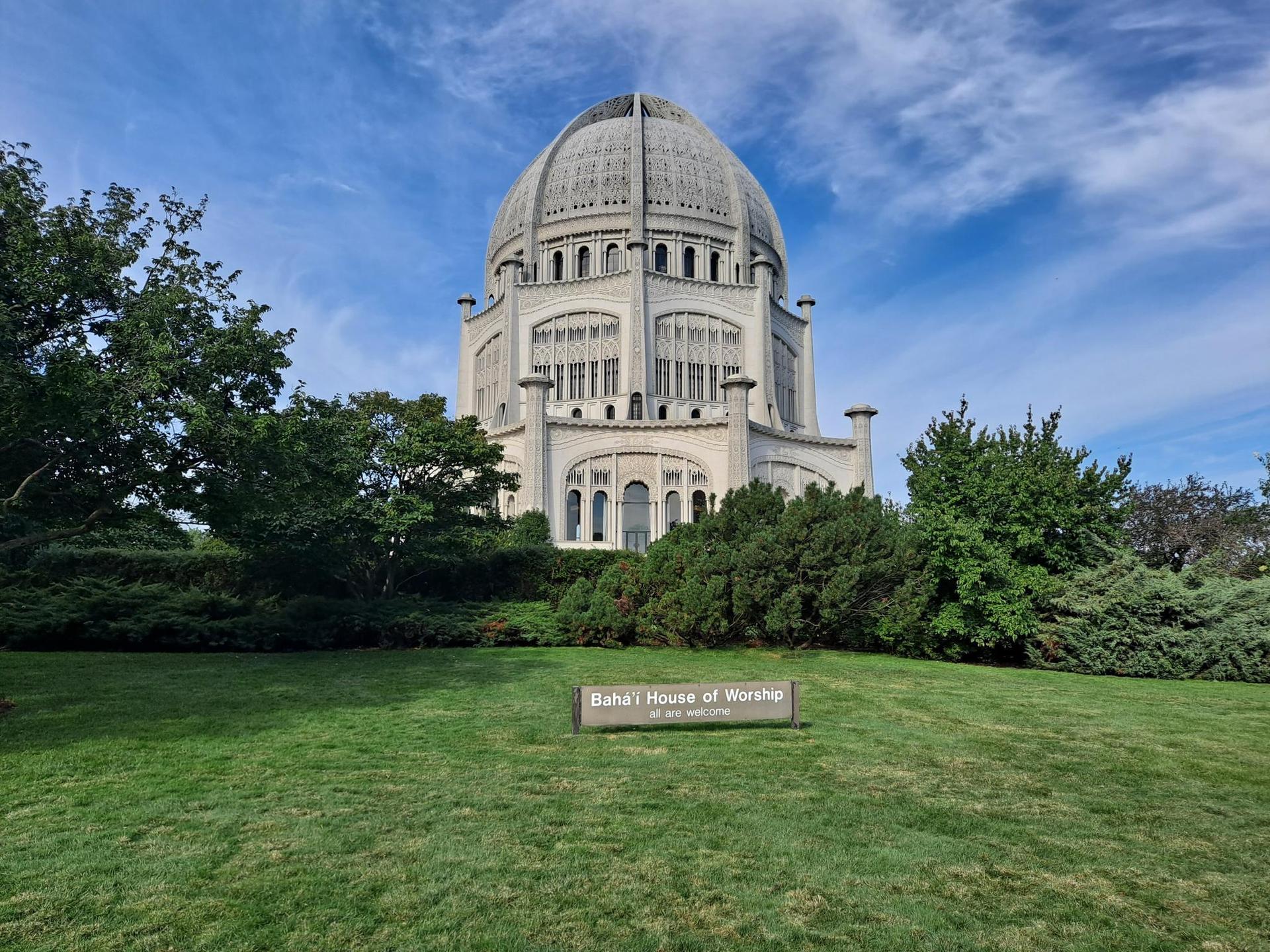 A grand white domed building on a green hill under a bright blue sky.