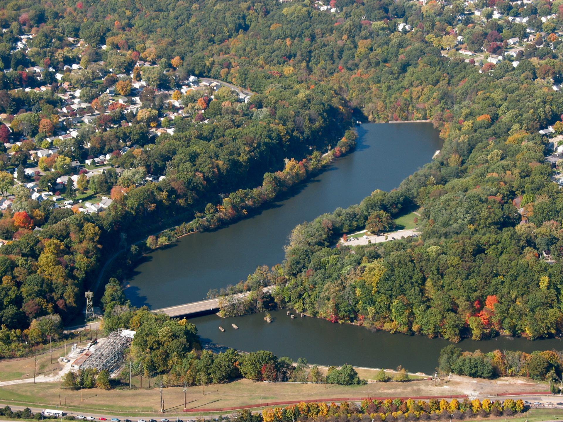 Aerial view of a winding river, dense forests, and scattered houses under bright sun.