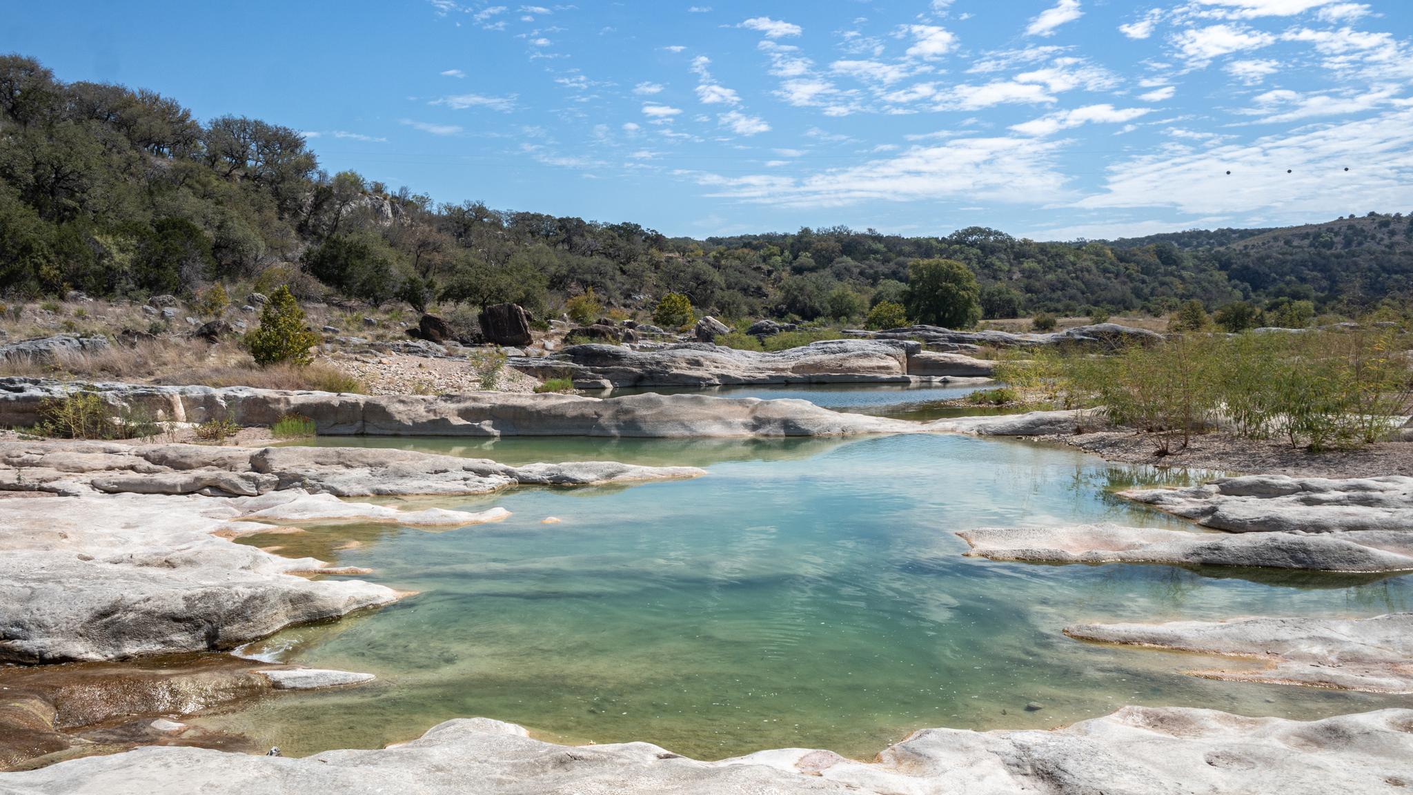 Sunny view of clear blue-green pools in a rocky riverbed.