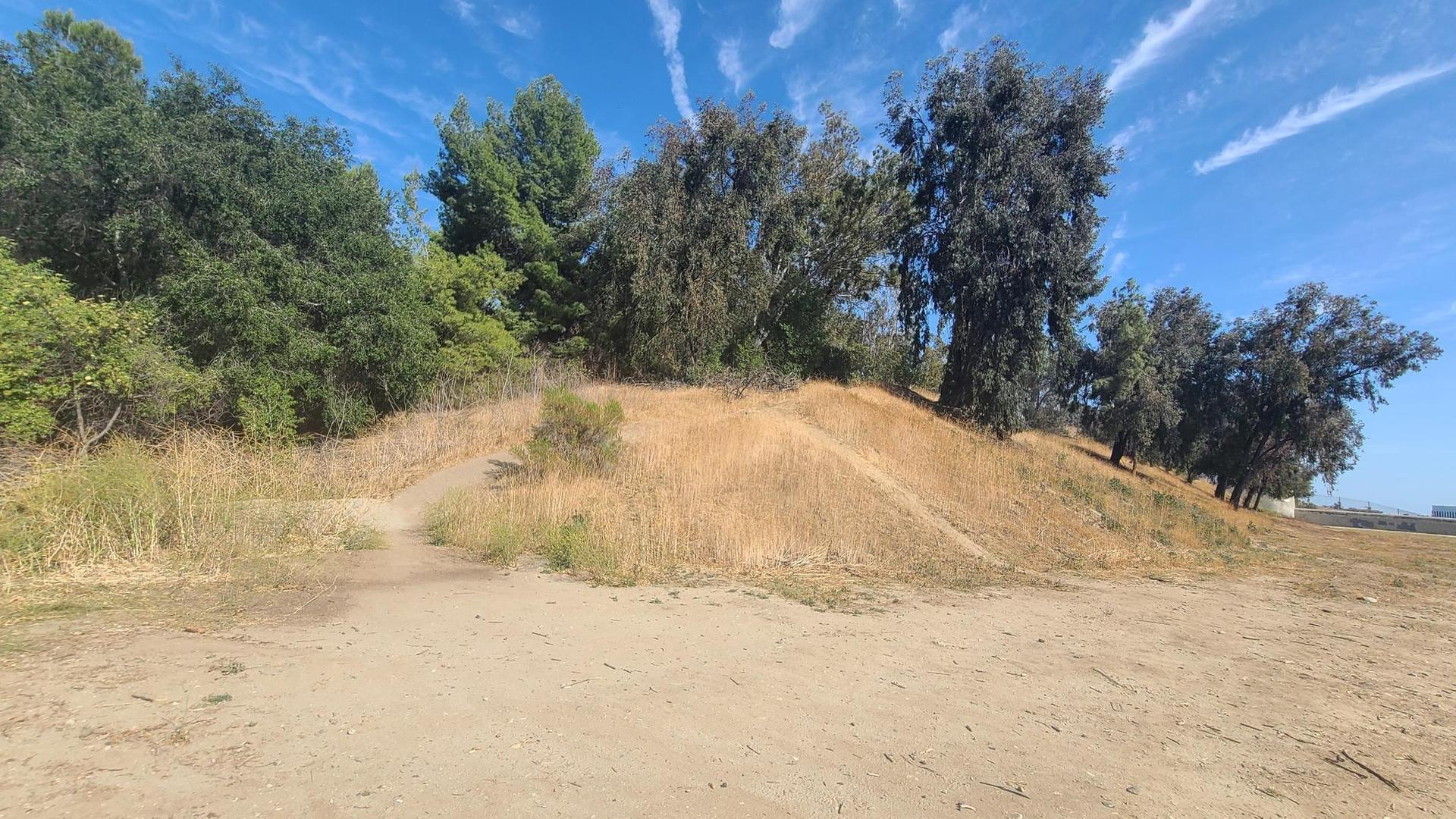 A dirt path leads up a dry, grassy hill under a bright, sunny sky.
