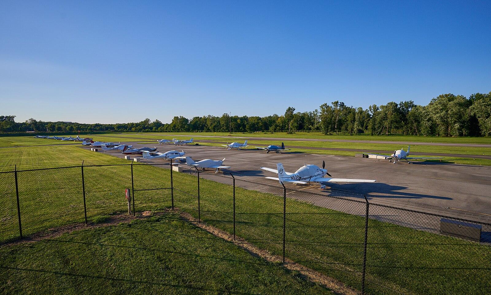 Small white airplanes parked on an asphalt runway under a clear blue sky.