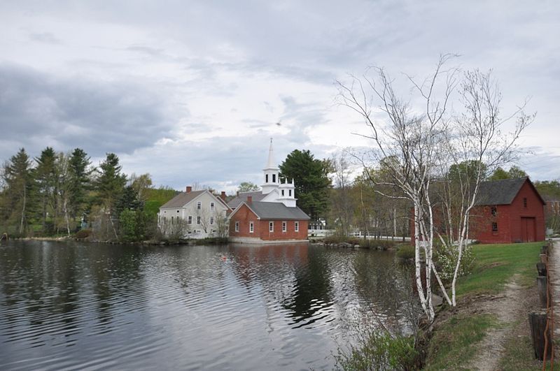 Historic buildings, including a red brick church, stand beside calm water under an overcast sky. - Harrisville loop from Dublin