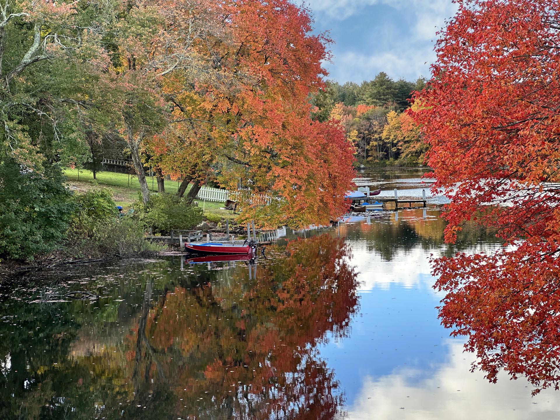 Vibrant autumn trees reflecting in calm water with a small red boat.