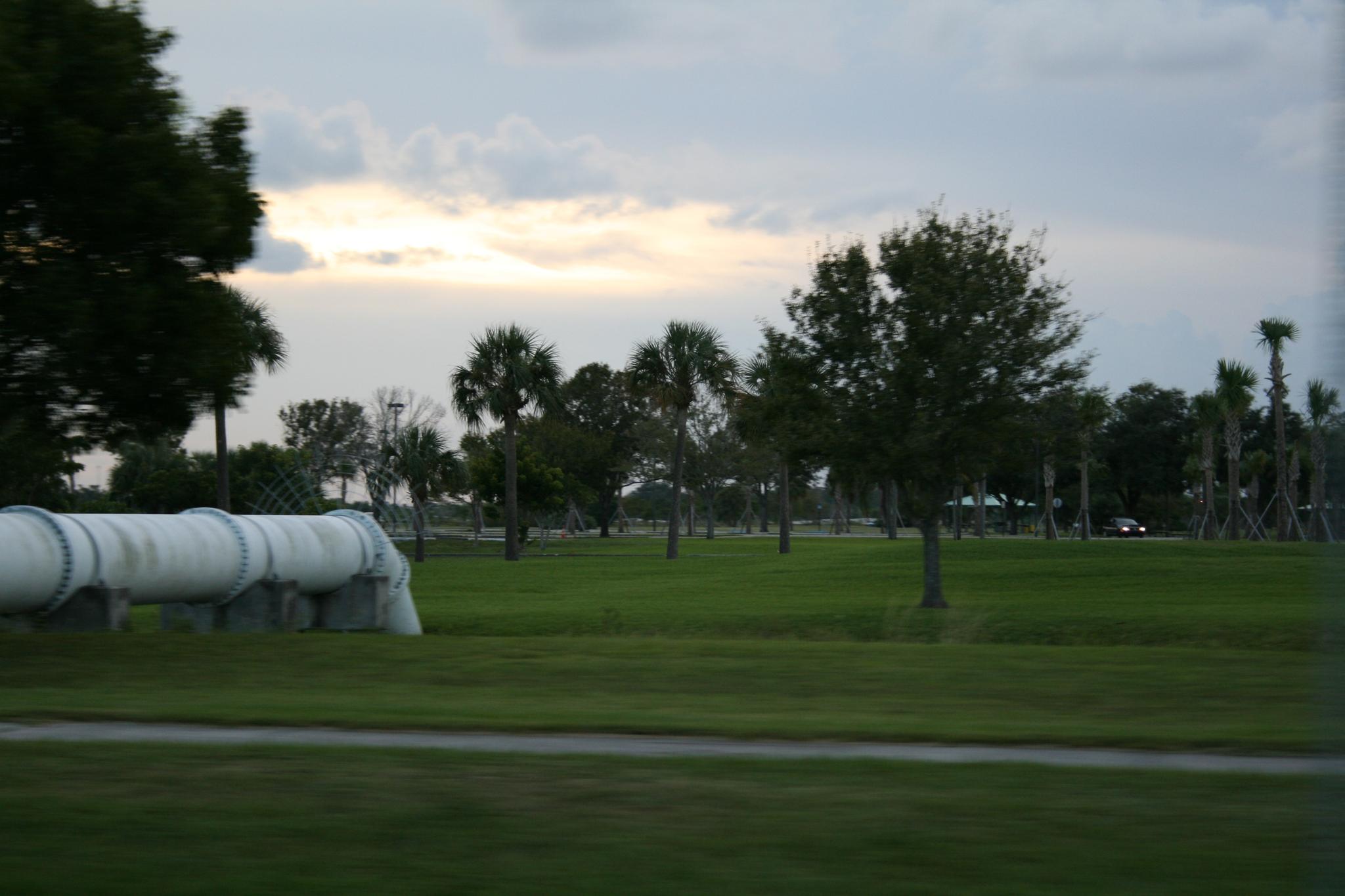 A large white pipe in a green field with trees under an overcast sky.