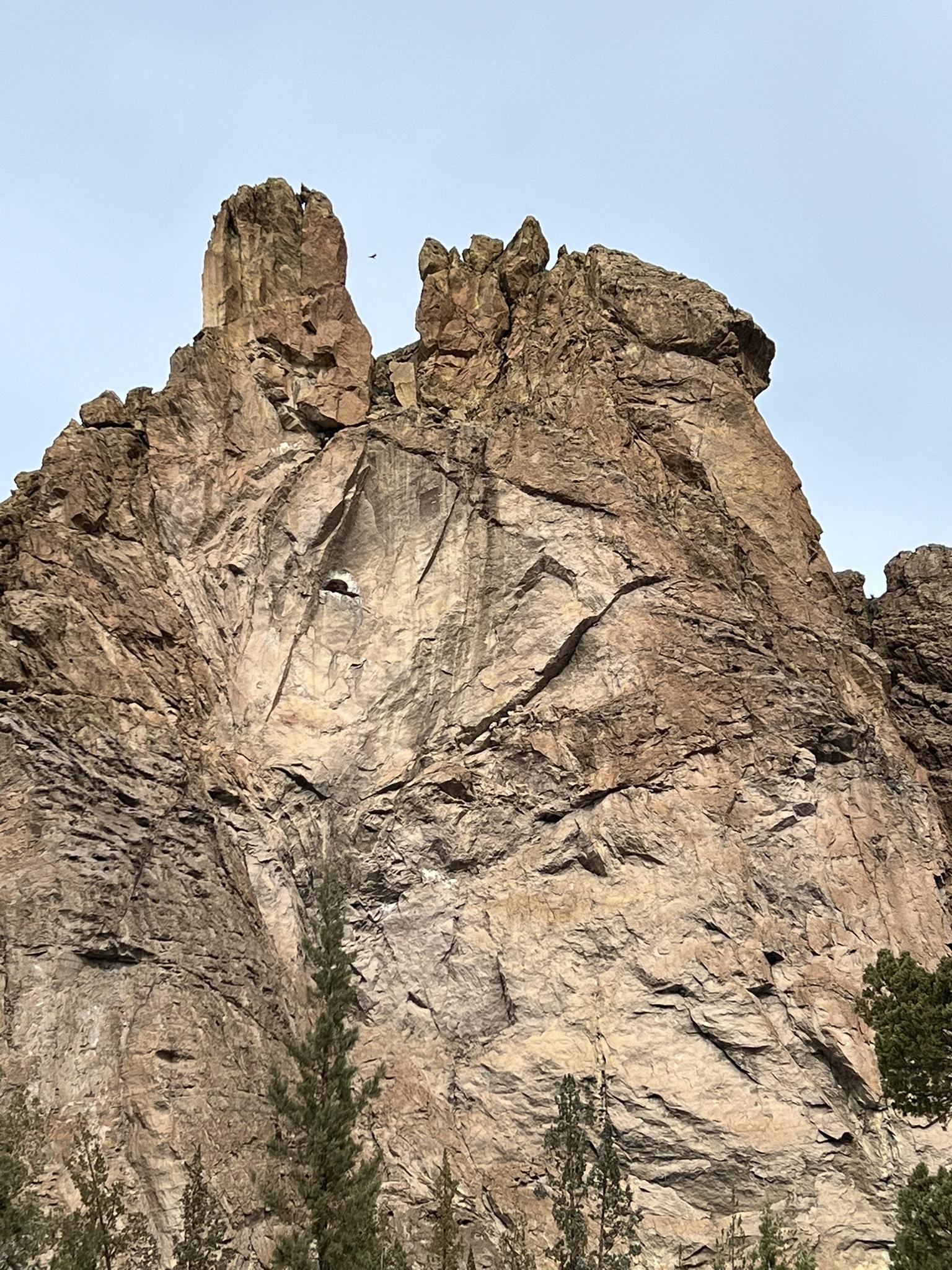 A towering, rugged rock formation with textured cliffs under an overcast sky.