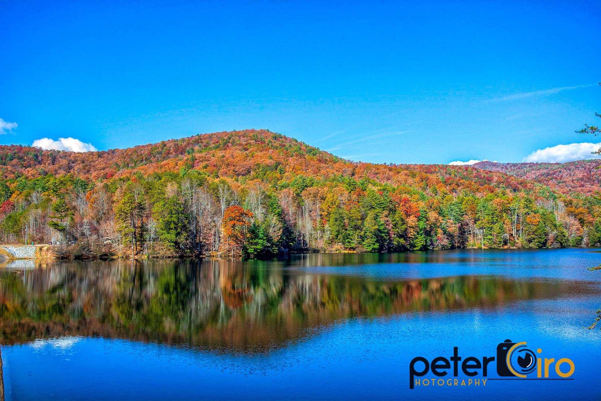 Vibrant autumn trees reflected in a calm, clear blue lake.