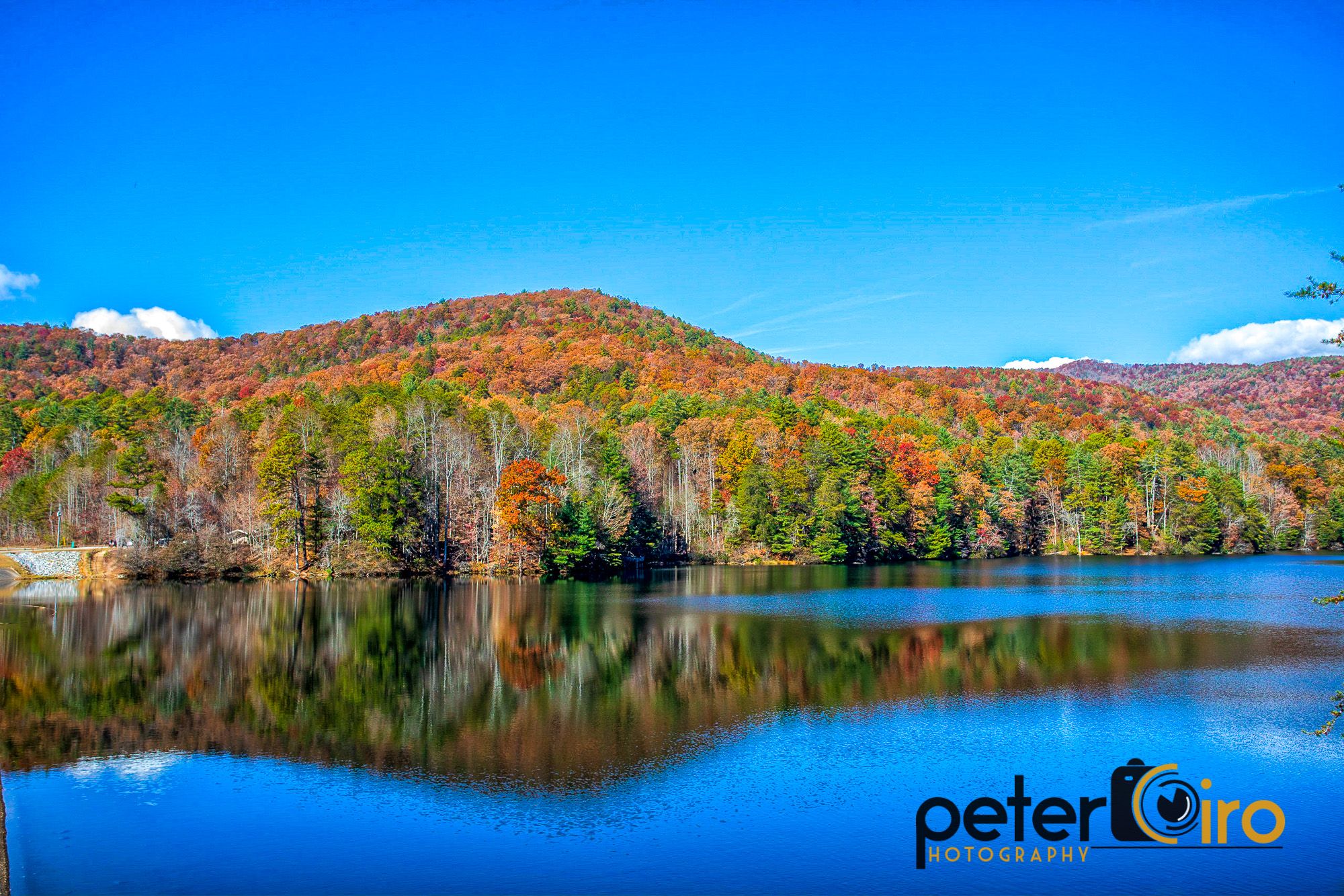 Vibrant autumn trees reflected in a calm, clear blue lake. - Unicoi Lake – Helen Bavarian Village loop from Helen