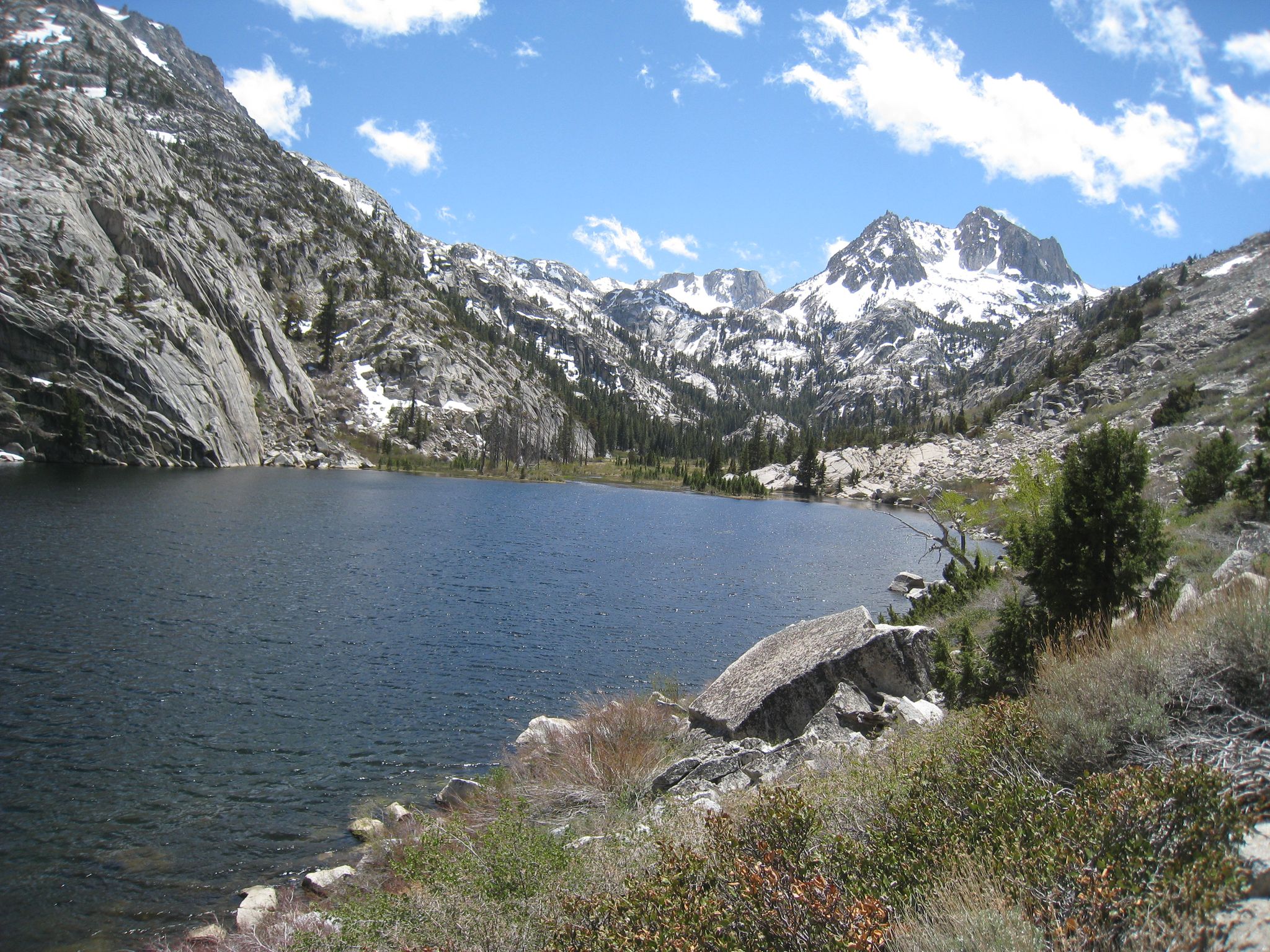 Alpine lake surrounded by rocky, snow-capped mountains under a bright, partly cloudy sky. - Barney Lake via Robinson Creek Trail