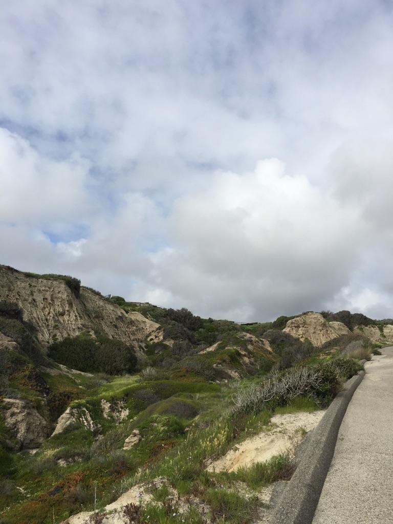 Green, rugged hills and a concrete path under a cloudy sky.