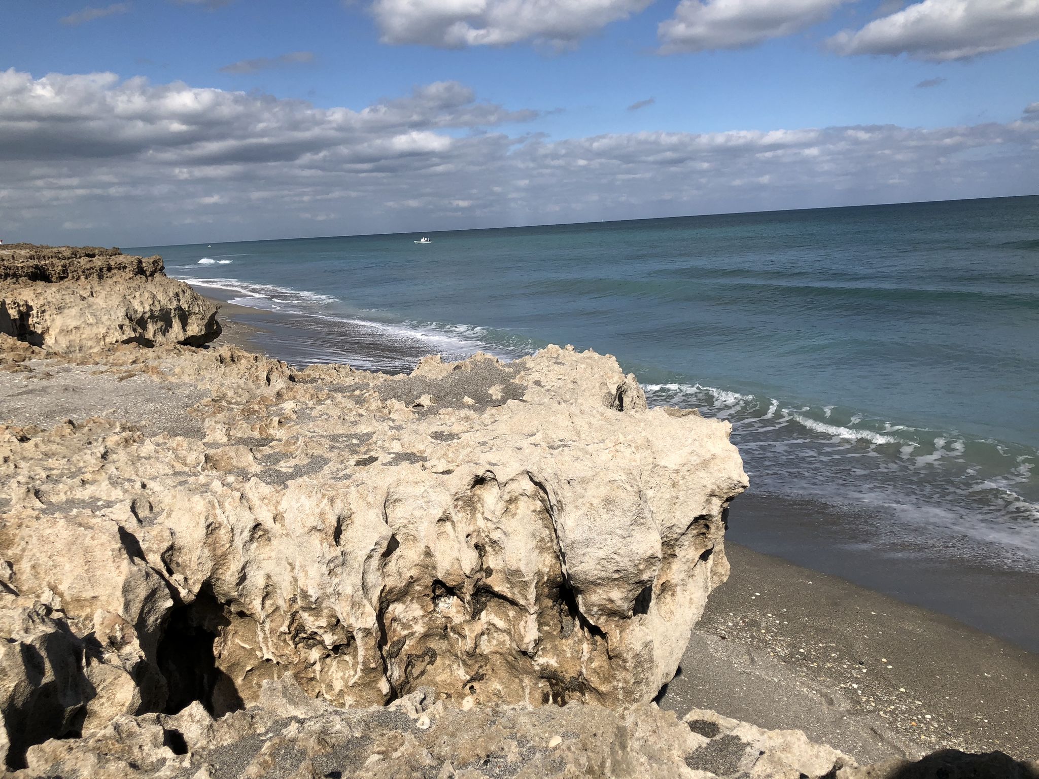 Rugged rocky coastline meets a sandy beach and blue ocean under a cloudy sky. - Jupiter loop from Roger Dean Stadium