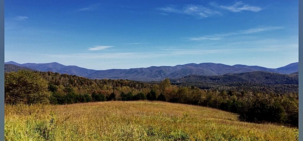 Vast mountain range and forested hills under a clear blue sky.