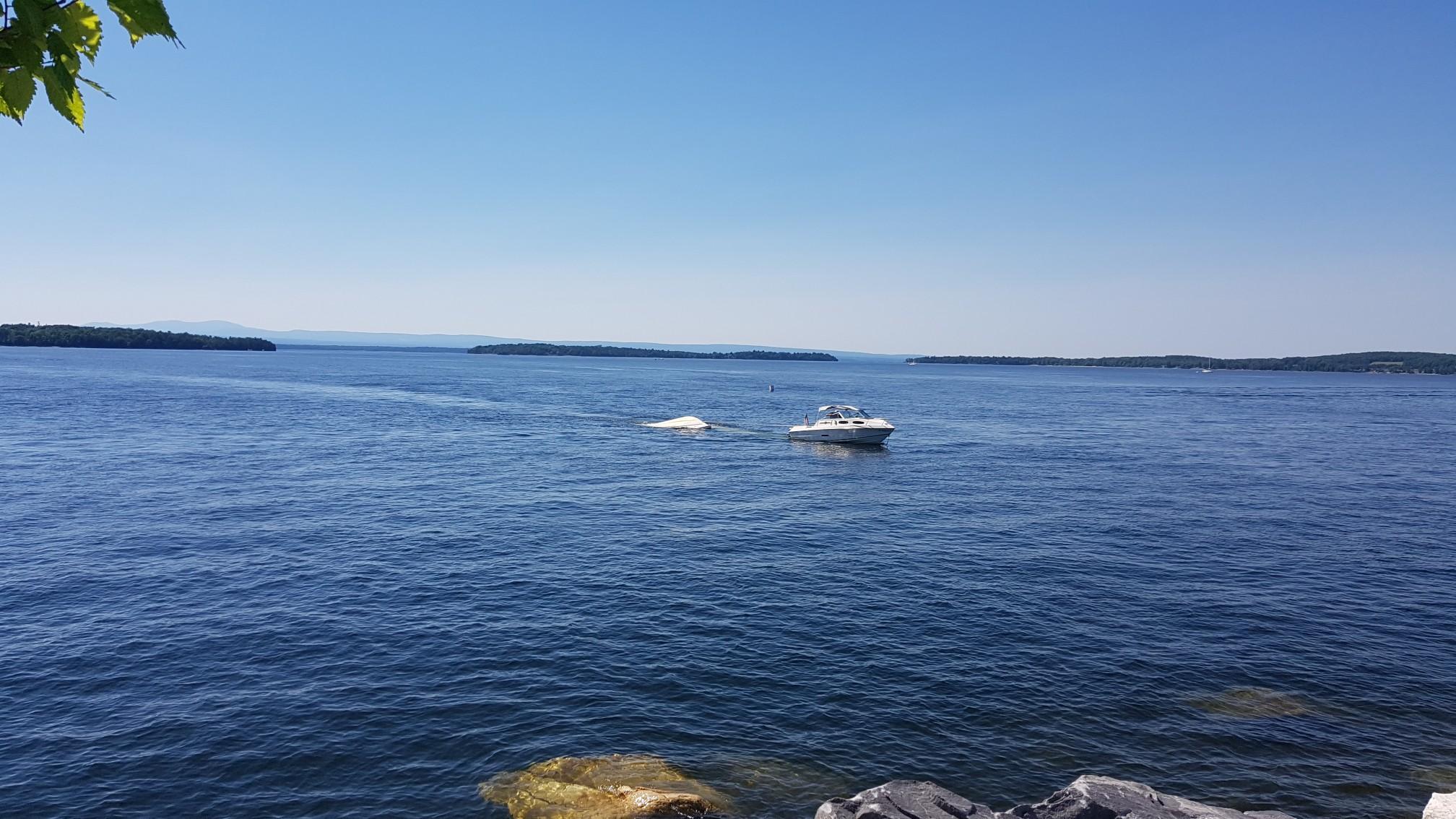 A motorboat pulling a tube on a wide, sunny lake with distant islands.
