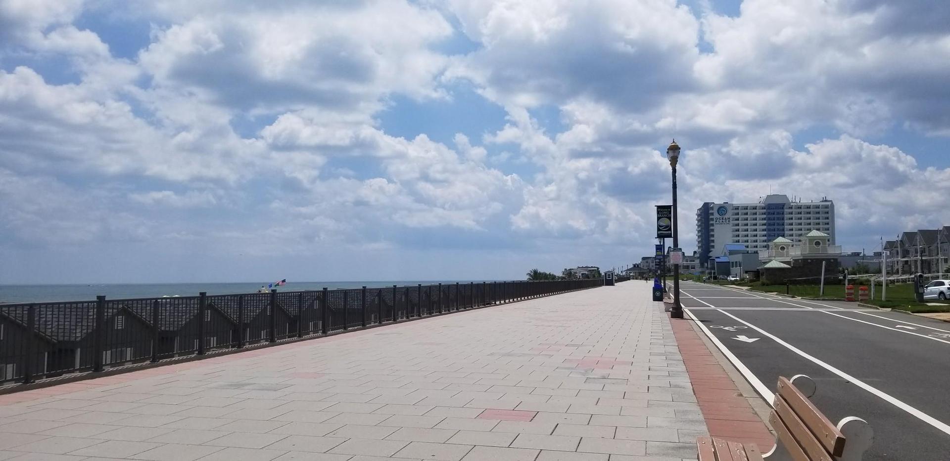 A wide boardwalk and road beside the ocean under a partly cloudy sky.