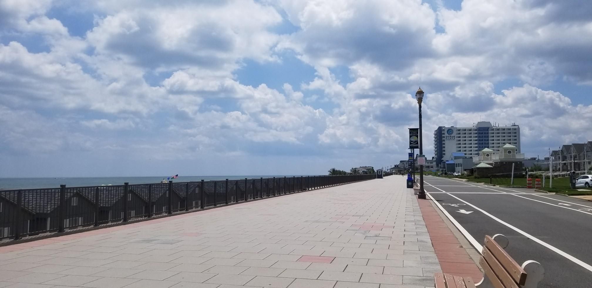 A wide boardwalk and road beside the ocean under a partly cloudy sky. - Long Branch Boardwalk