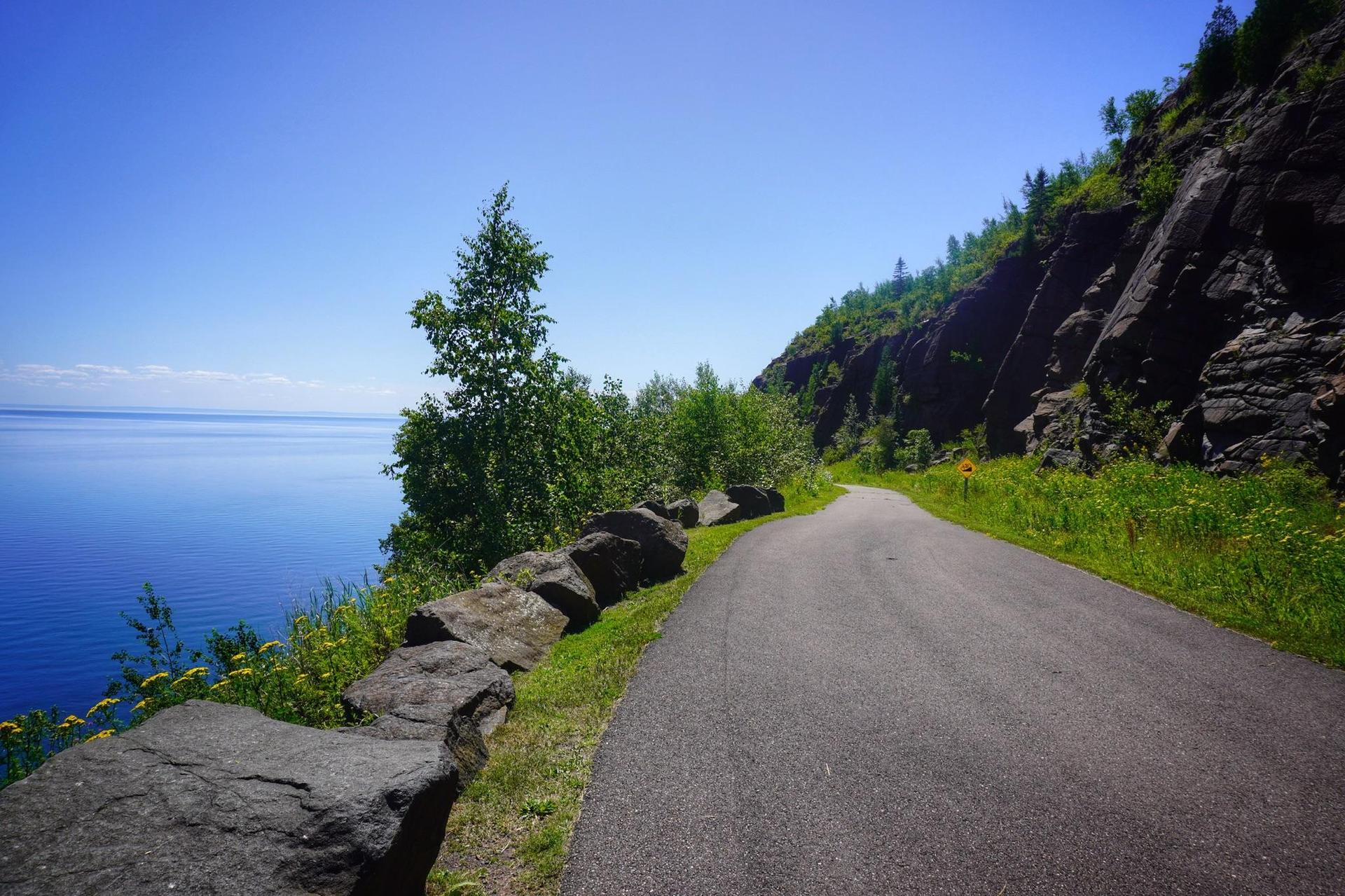 Paved road curves along a rocky coast with a vast blue sea.