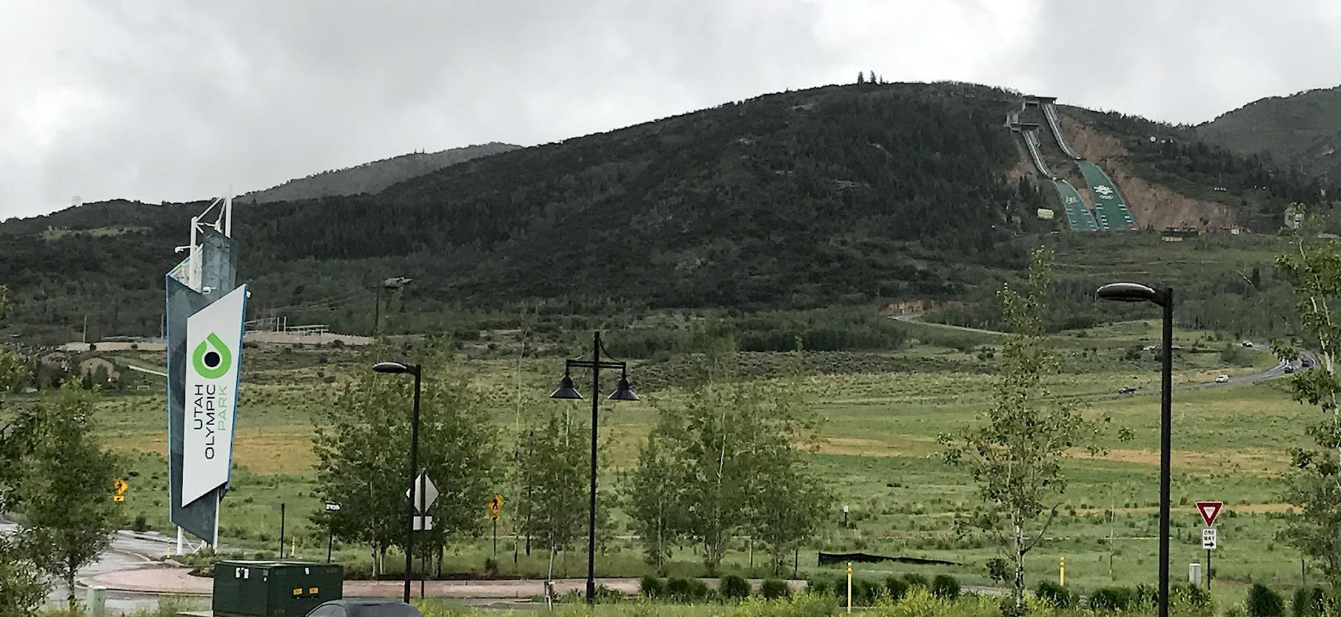 Overcast view of a green mountain with ski jumps and a large banner.