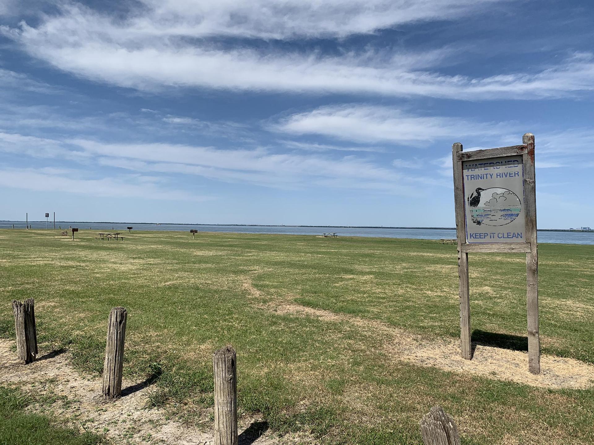 Grassy field with a wooden sign, wooden posts, and a large body of water.