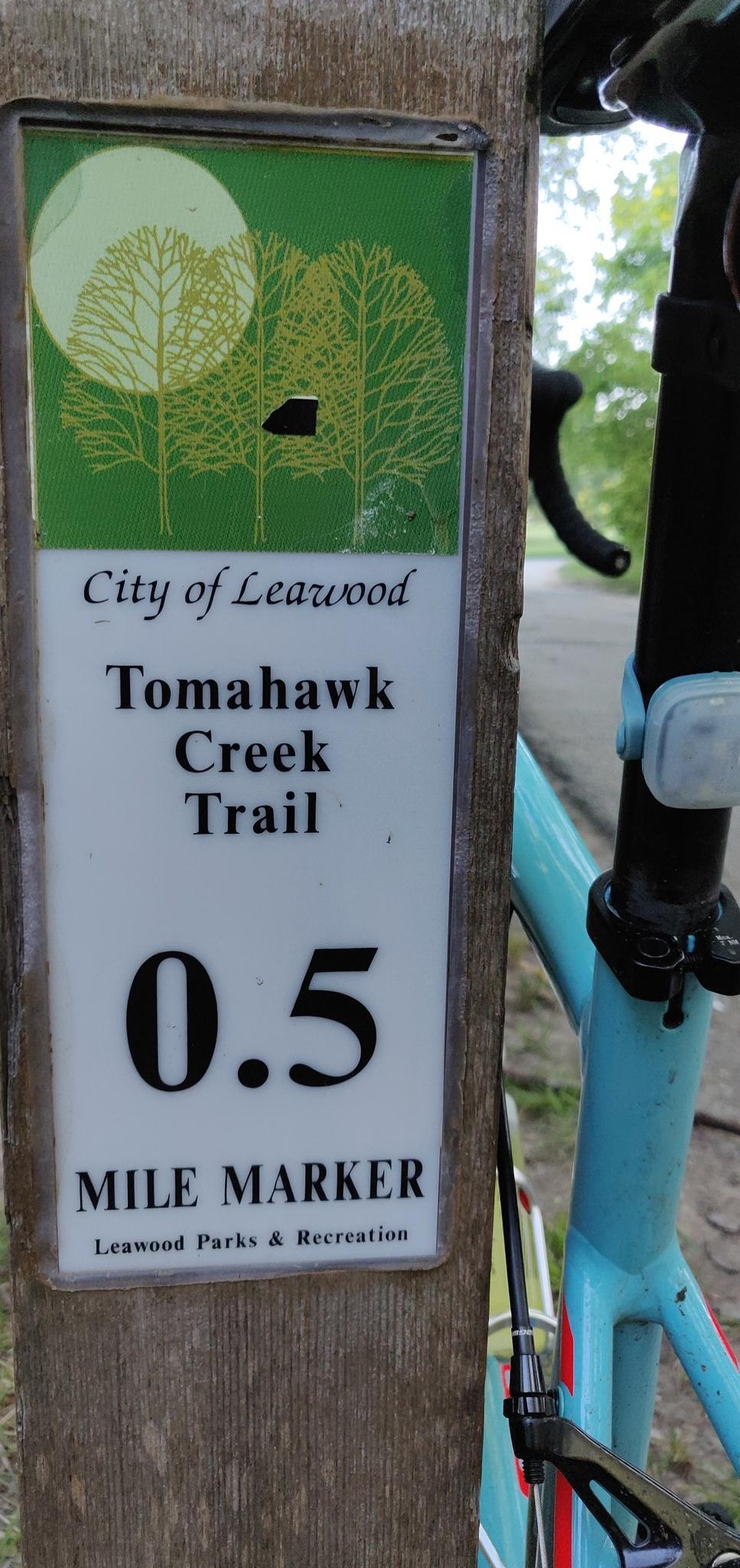Close-up of a trail marker sign on a wooden post next to a bike.