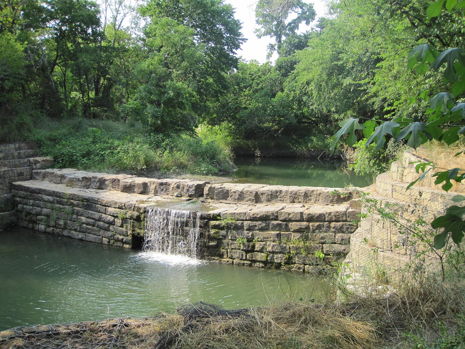 Stone dam with small waterfall in a lush green river landscape.