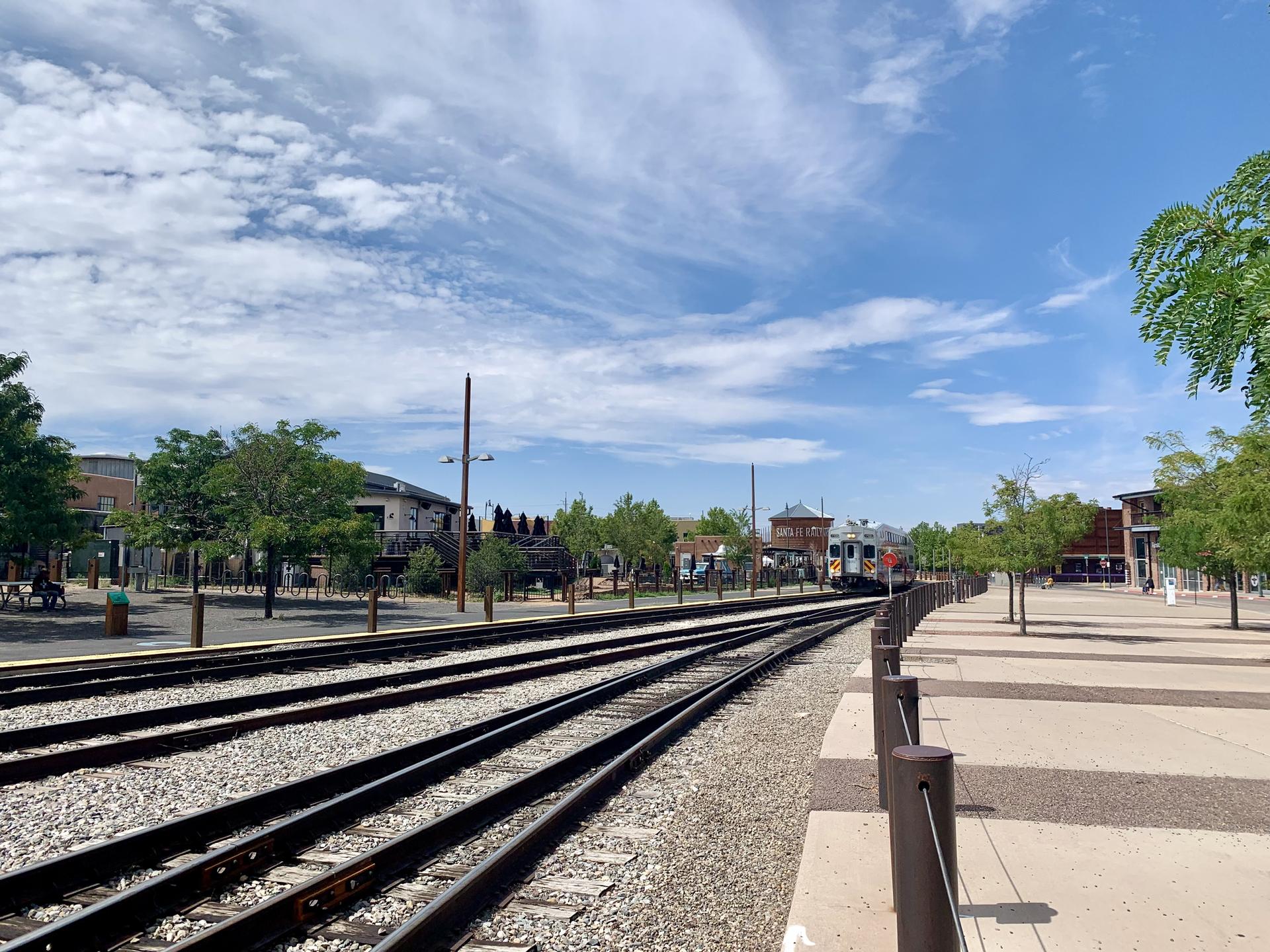 Multiple train tracks lead into a town with buildings and trees under a cloudy sky.