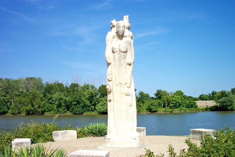 Tall white statue of a figure by a river under a bright blue sky. - Lawrence to Clinton State Park loop — Douglas County