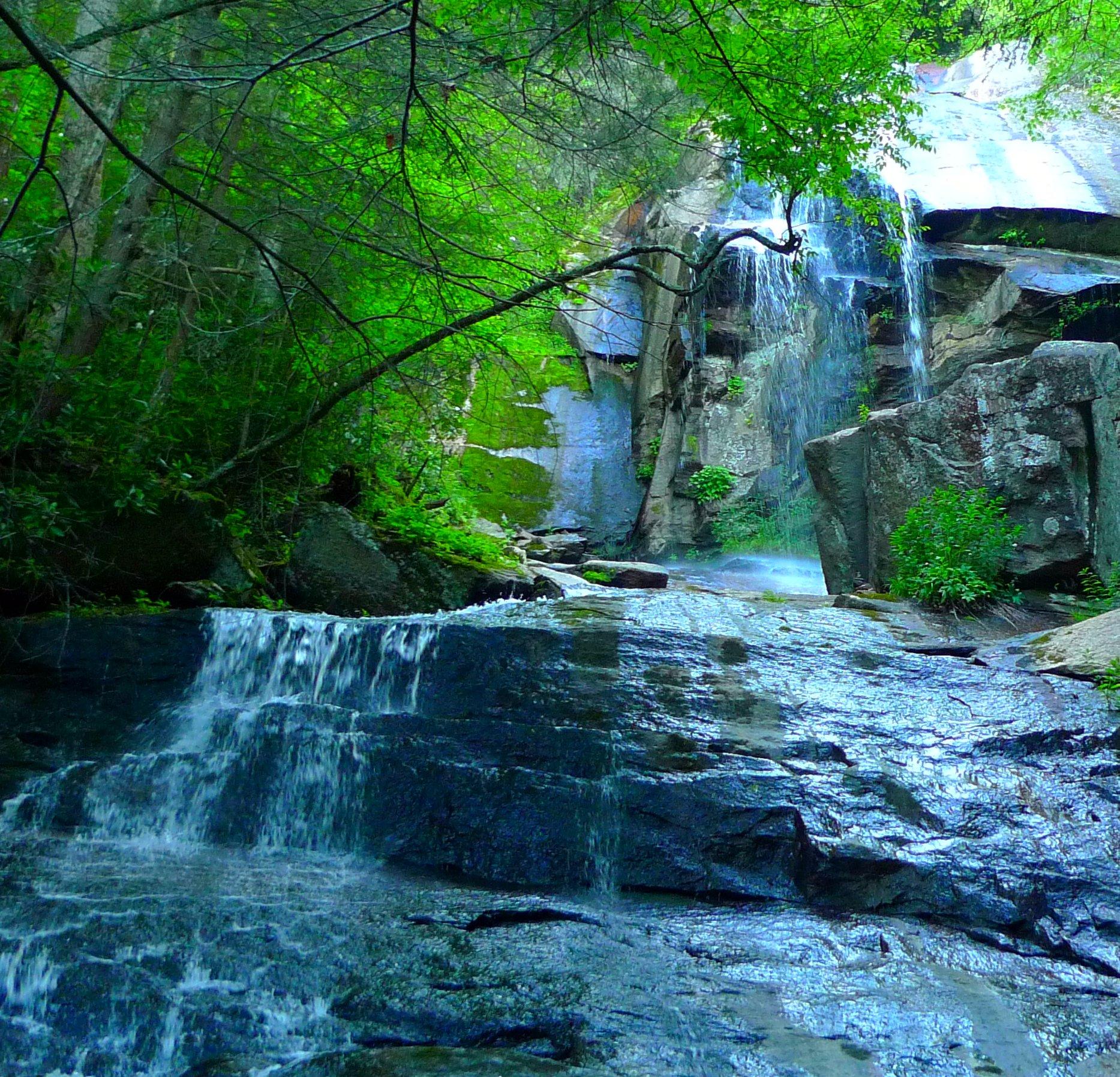 A multi-tiered waterfall flows through a vibrant green, rocky forest landscape.
