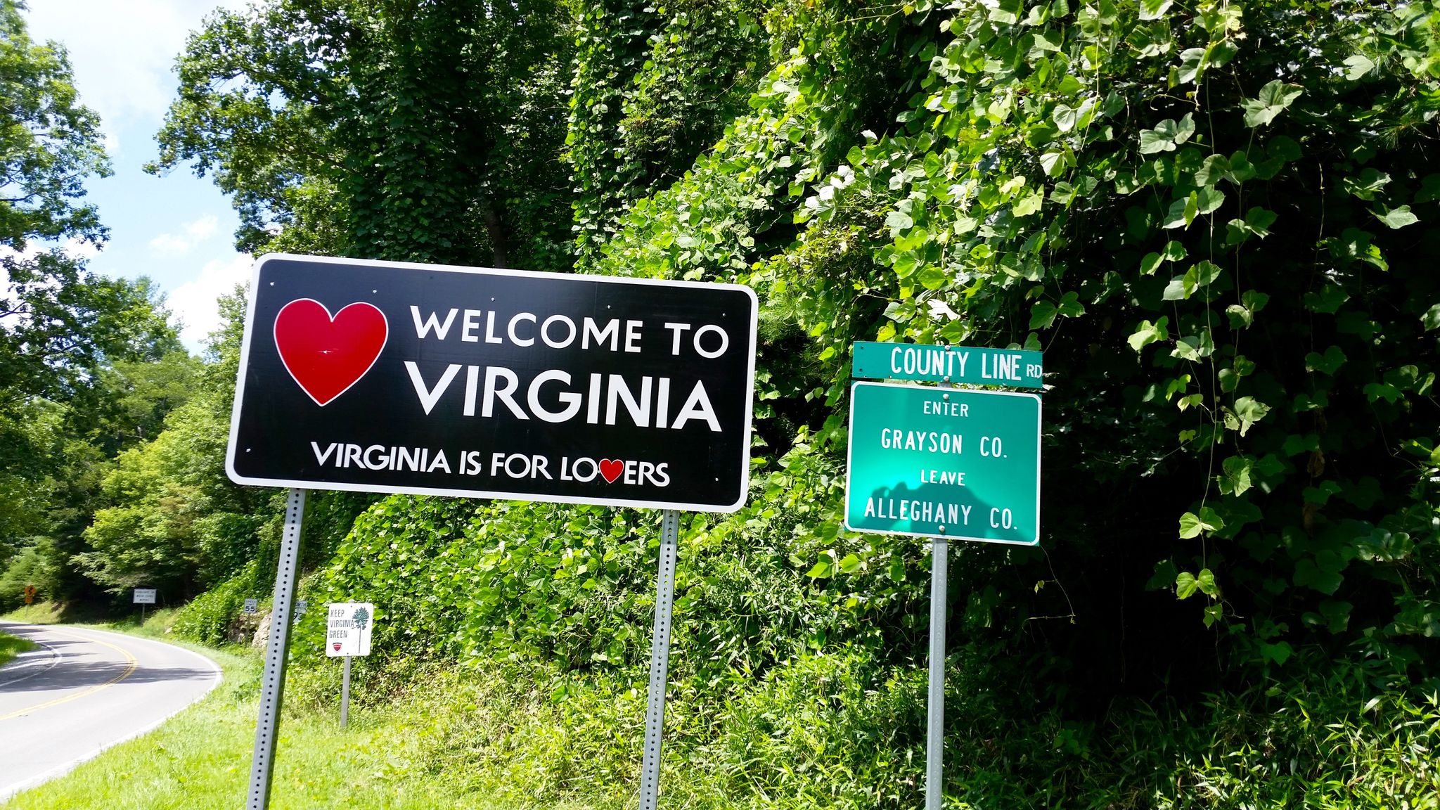 Two road signs, one welcoming to a state, surrounded by bright green foliage. - Red Dog Bar & Bistro to Stuart Dam