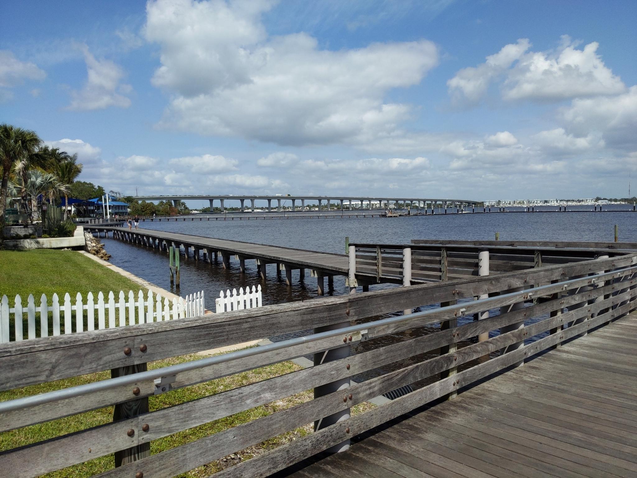 A long wooden boardwalk and pier extend over calm water under a bright sky.