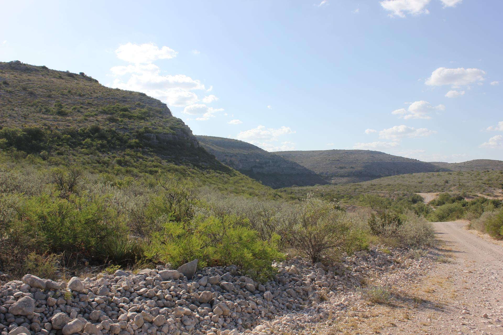 Dirt road next to rocky terrain, leading into a scrub-covered valley.