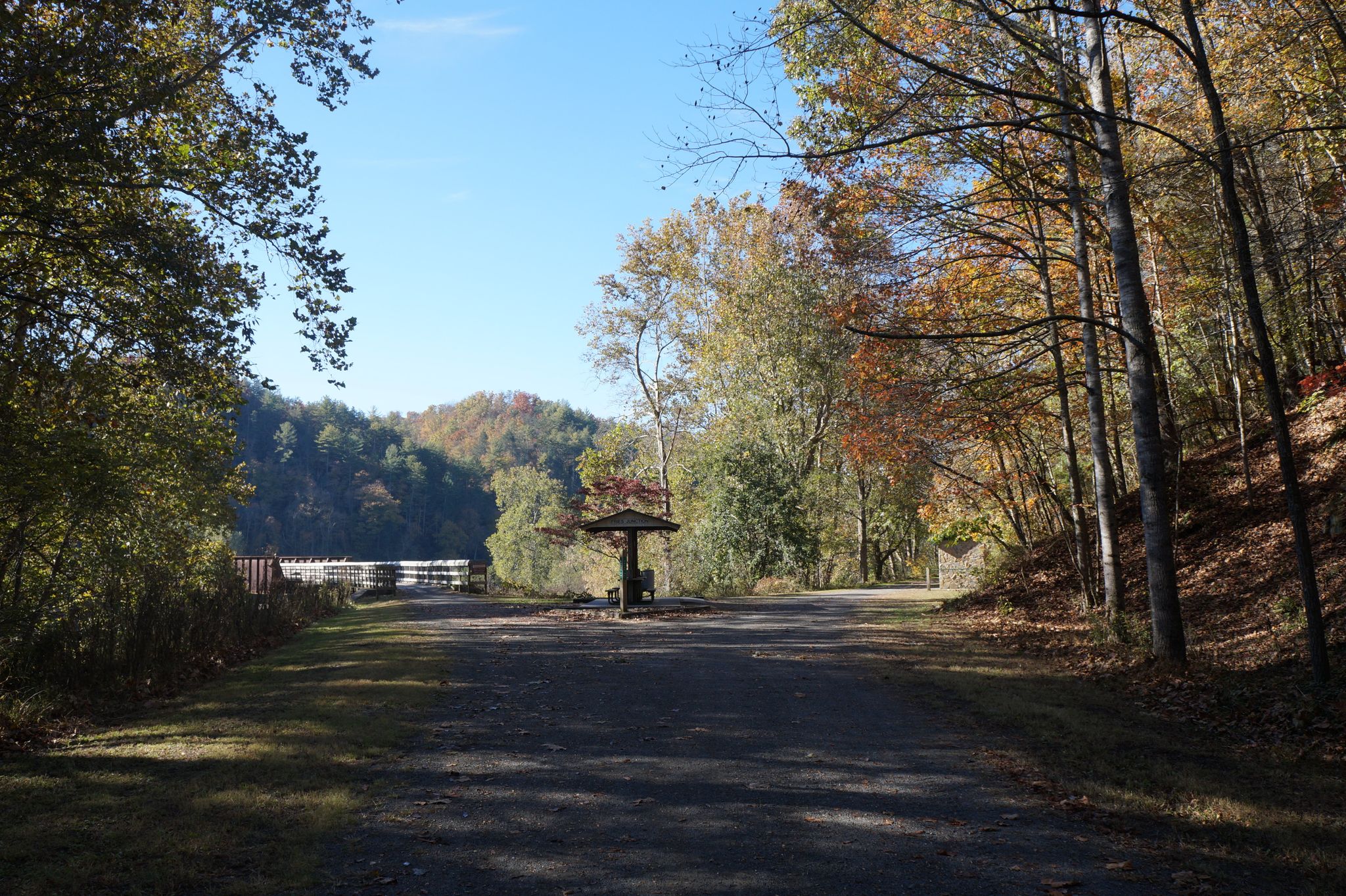 Paved path leading to a covered shelter, surrounded by autumn trees. - New River Trail