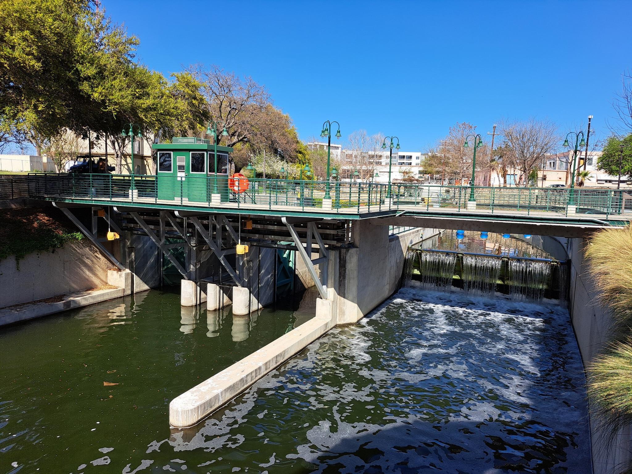 River flowing over a dam with a green control booth and bridges.