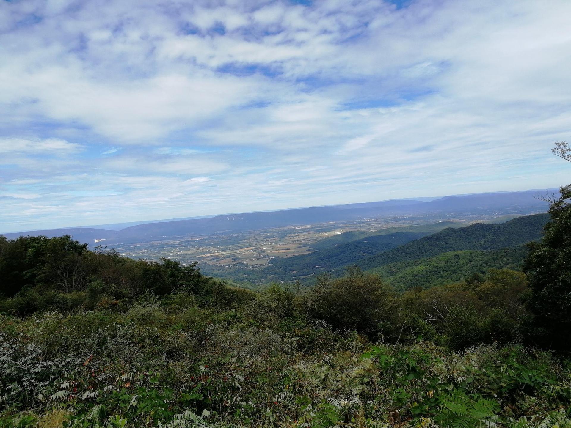 Panoramic view of green mountains and a wide valley under a partly cloudy sky.