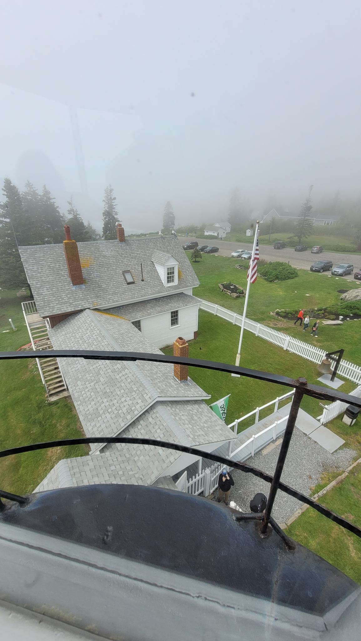 Foggy aerial view of buildings, a flag, and a parking lot with people.