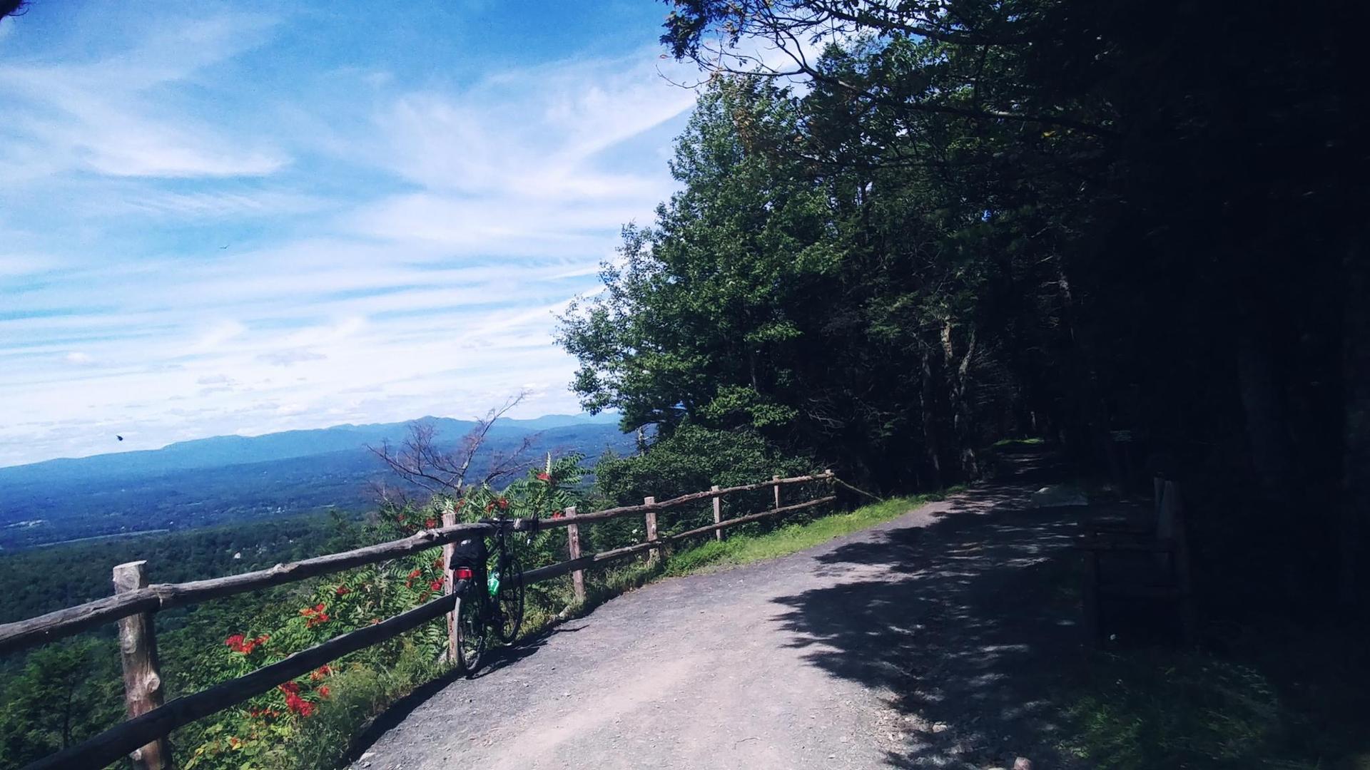A bicycle rests by a wooden fence overlooking a vast mountain landscape.