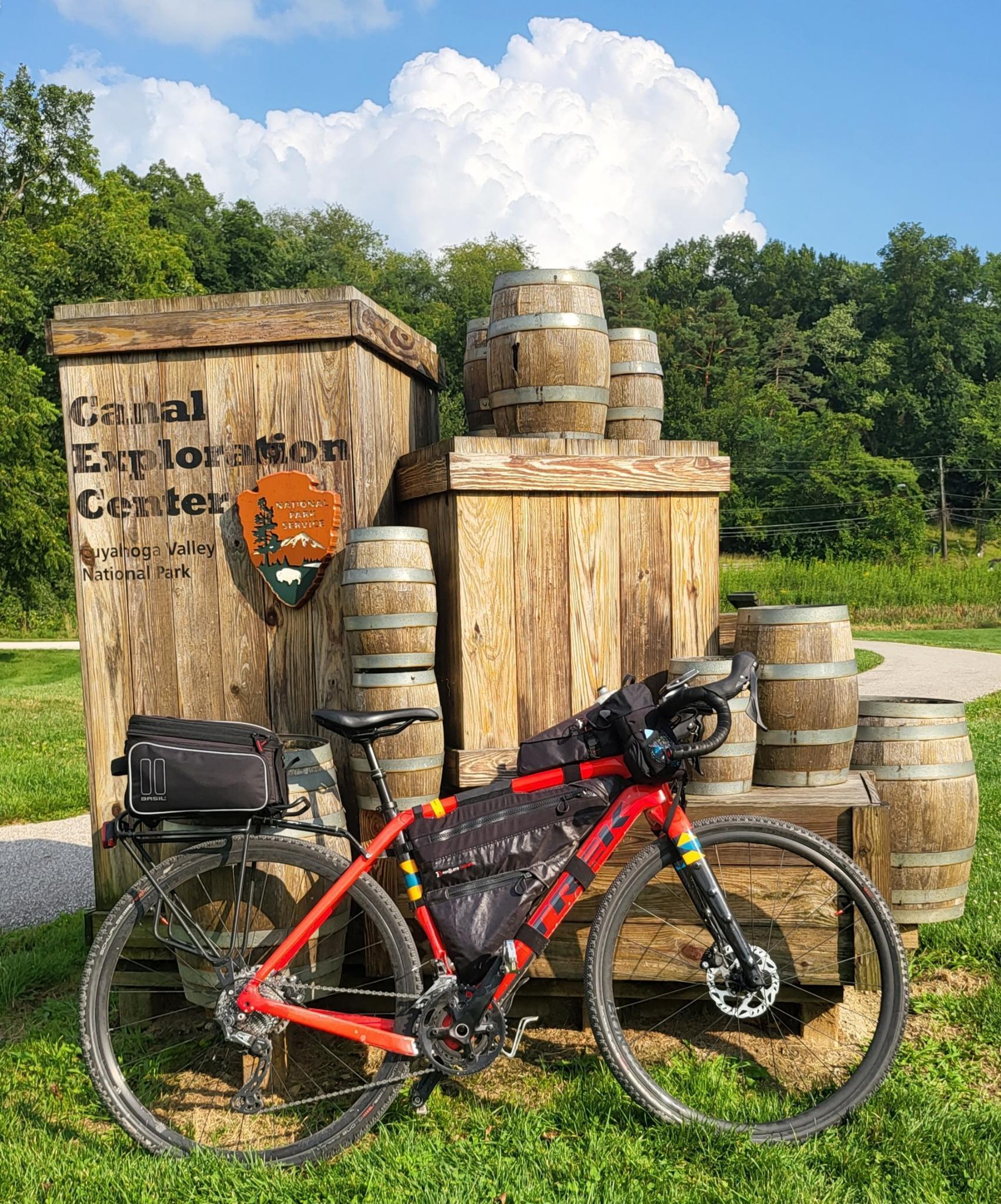 Red bikepacking bicycle parked in front of a wooden sign and barrels.