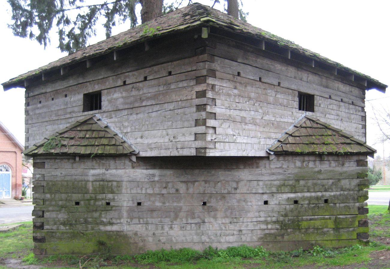 Weathered, moss-covered log structure with small windows under an overcast sky.