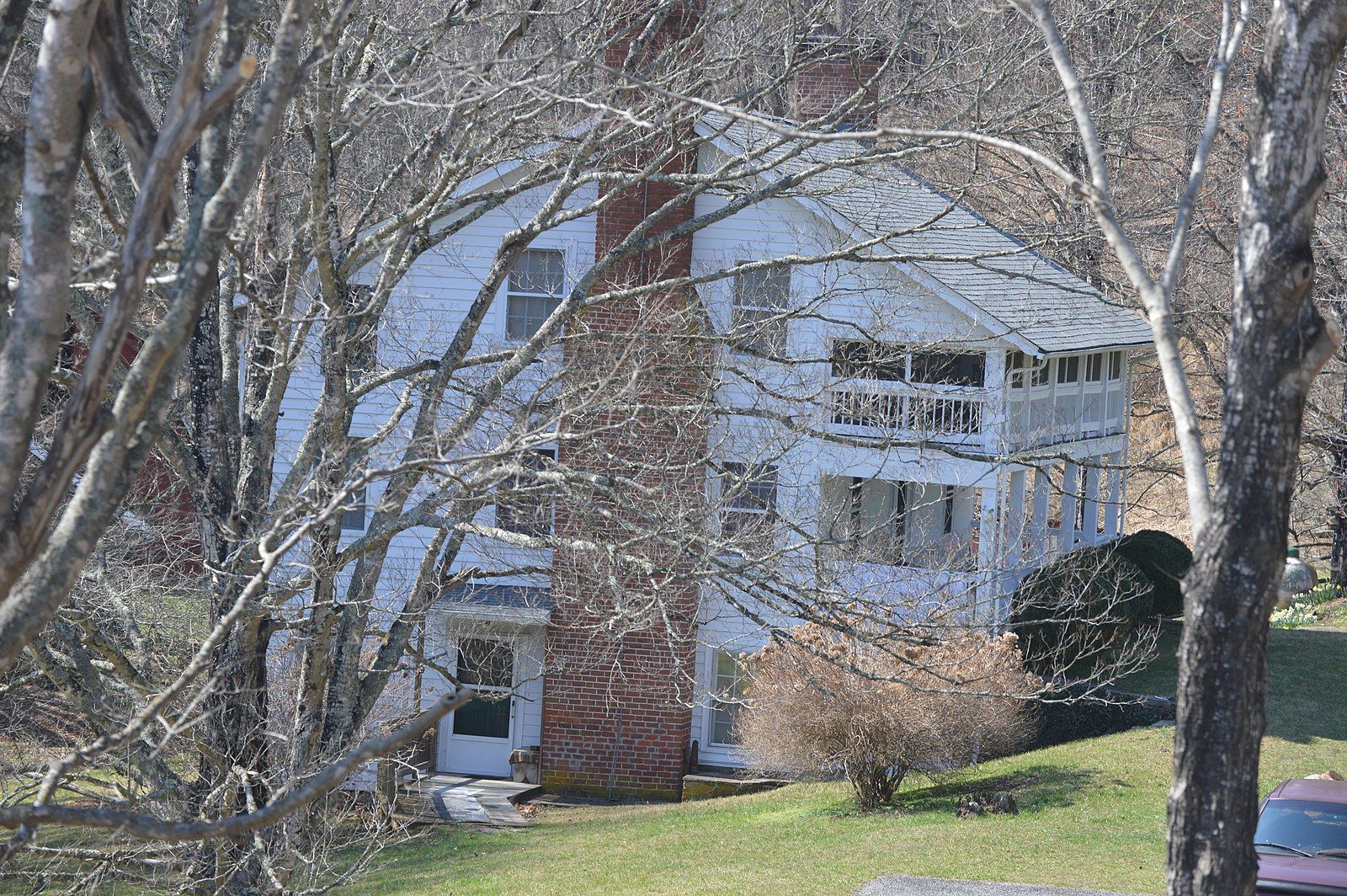 White house with a brick chimney, seen through bare winter trees on a sunny day. - Sparta and North Line Trace Loop
