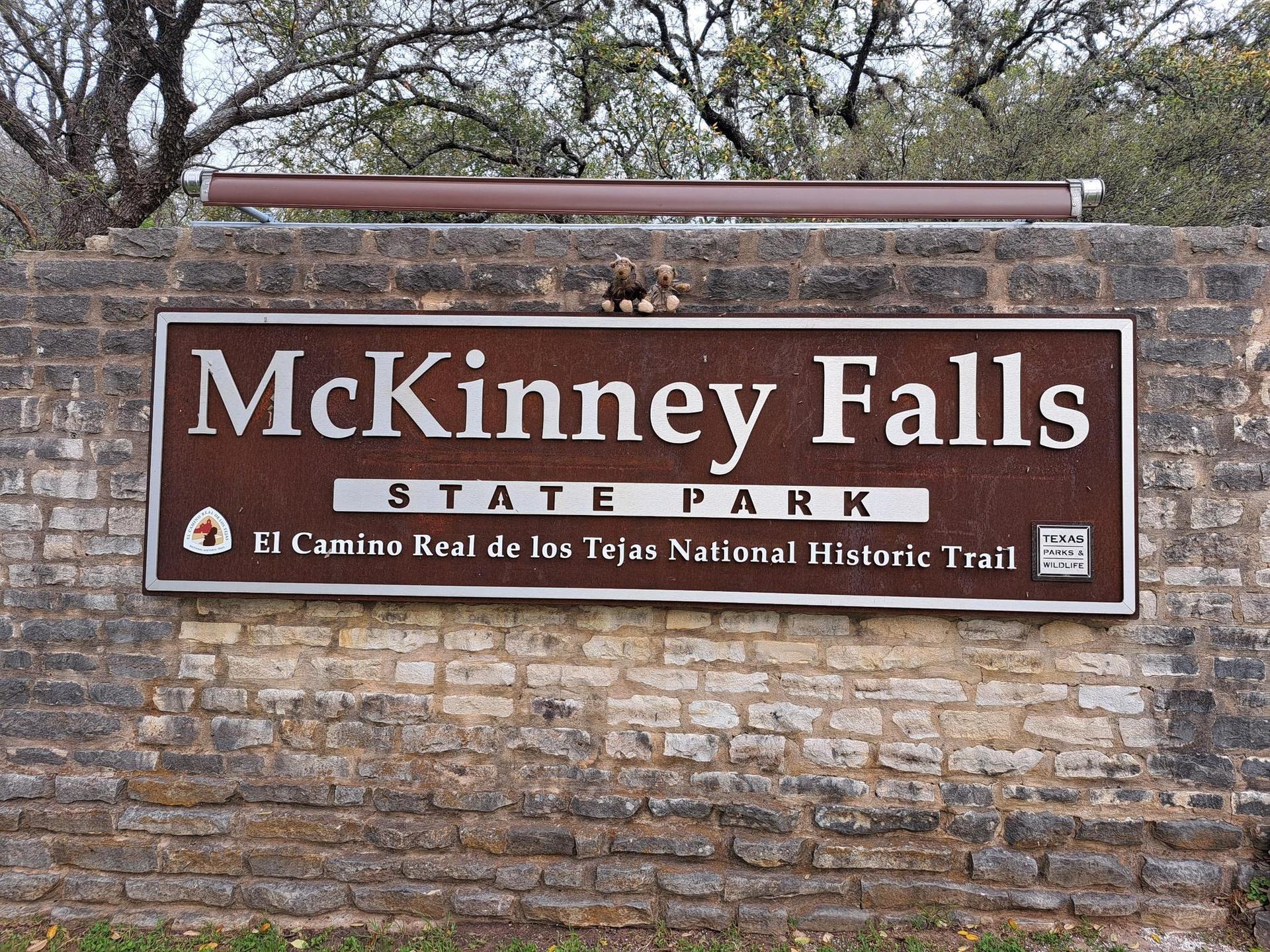 A large brown sign mounted on a textured stone wall.