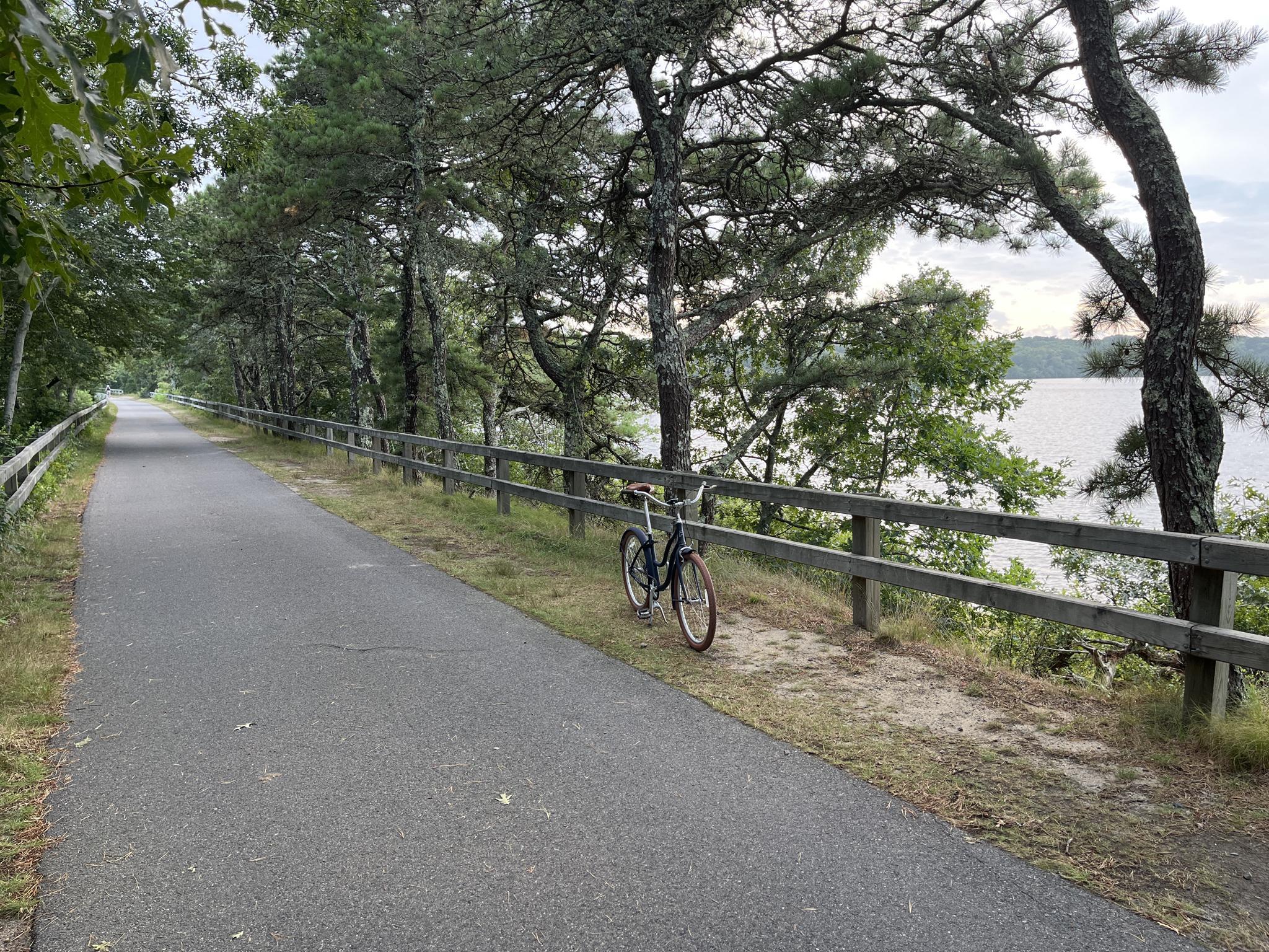 Paved path with a bicycle by a wooden fence and lake.