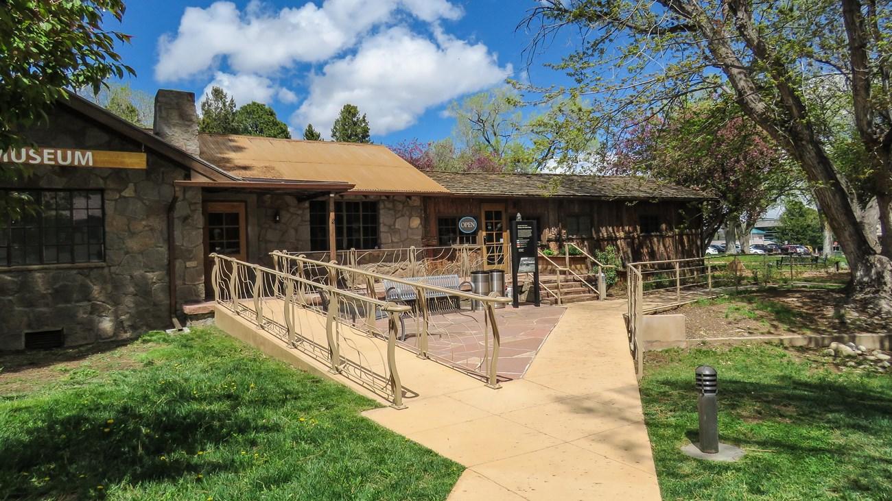 Stone building with an accessible ramp leading to a patio area on a bright day.