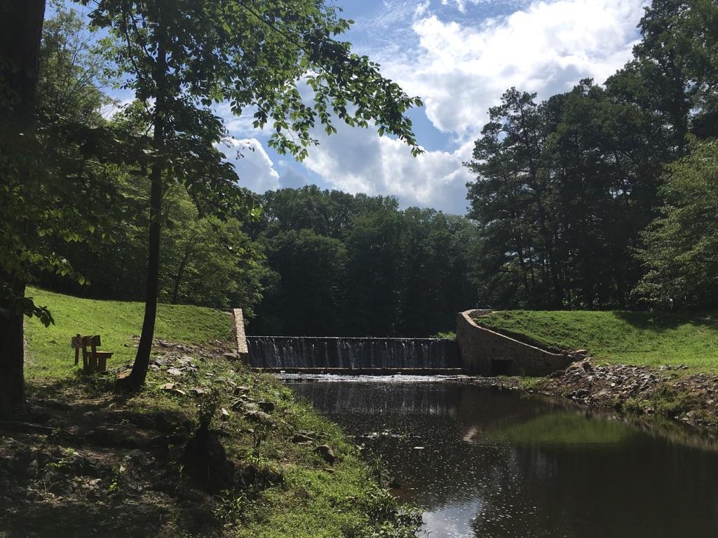 Small waterfall flowing into a river, surrounded by green trees under a bright sky.