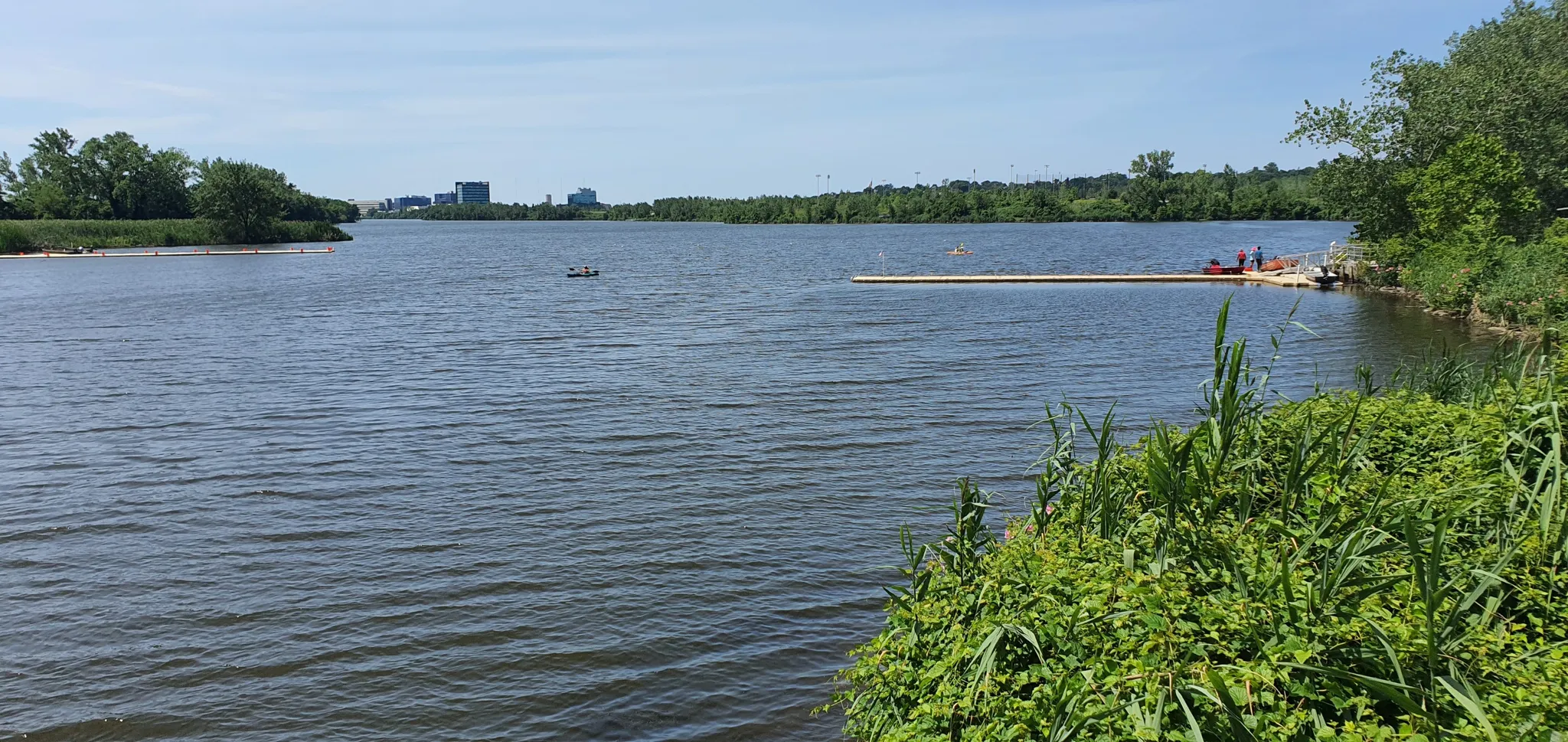 Wide river with a dock and distant city skyline under bright daylight. - Overpeck Park River Loop
