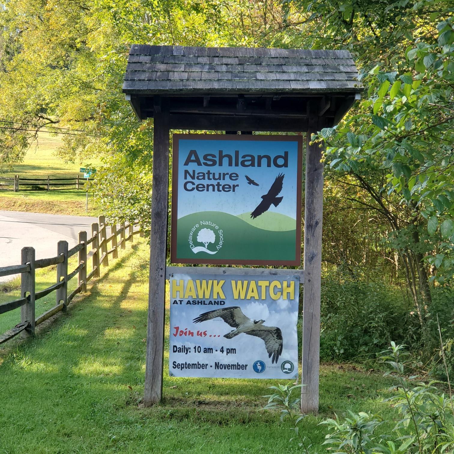 Wooden signpost with nature center and hawk watch signs in a grassy area.