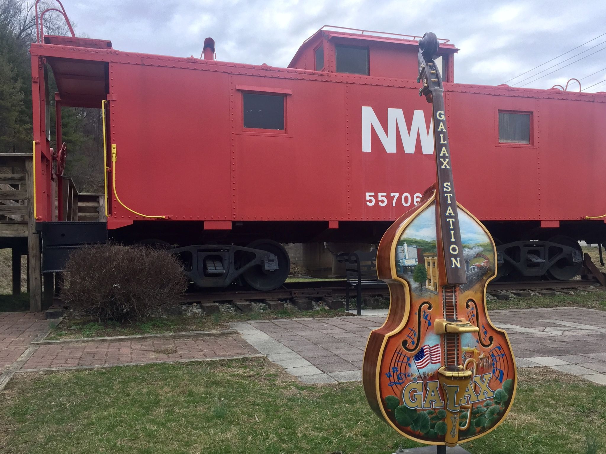 Decorative upright bass sculpture in front of a red train caboose on tracks. - Galax – New River Trail loop from Dannelly Park