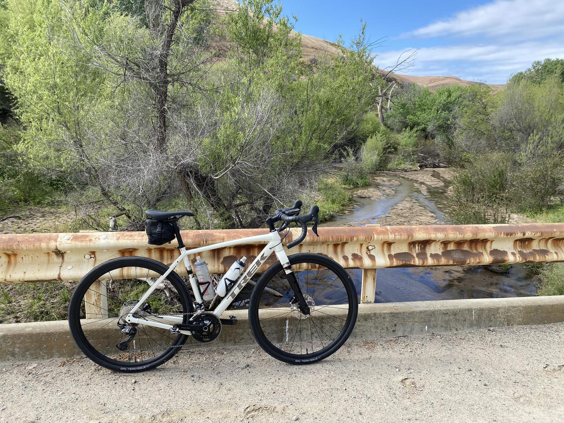 White bicycle rests on a rustic bridge over a stream on a sunny day.