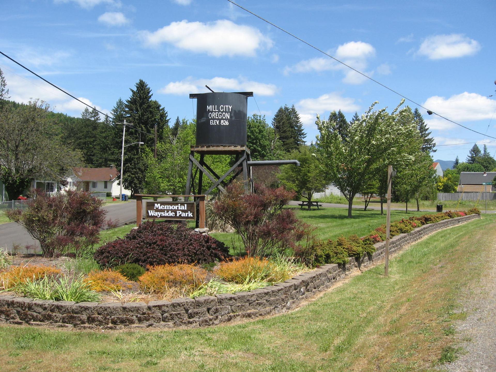 A black water tower, park sign, and landscaped garden on a bright, sunny day.