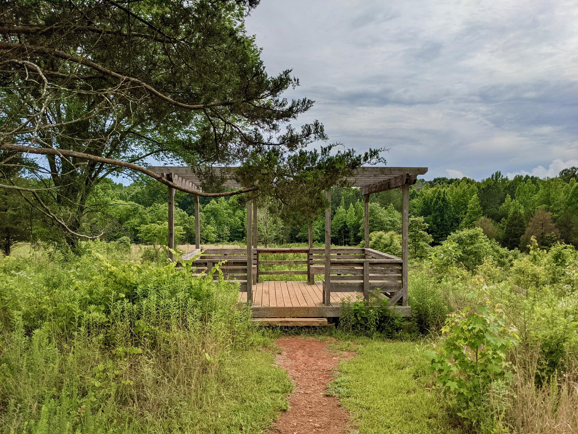 A wooden observation deck in a lush green field under an overcast sky.